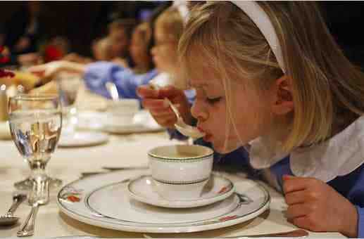 一个年轻的金发女孩在喝汤。