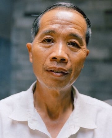 一名中国男子盯着镜头，脸上没有笑容。