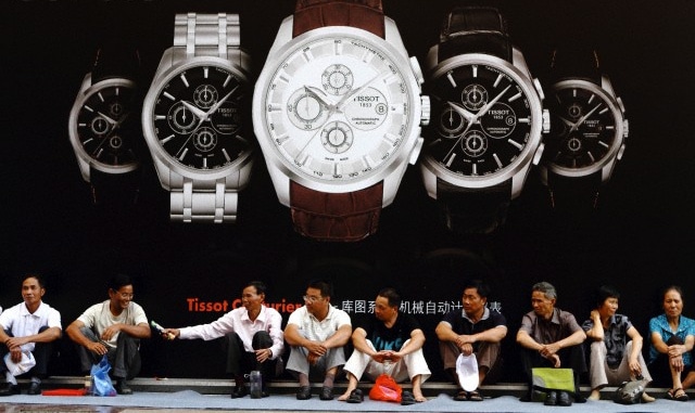 一群中国男人坐在一块花哨的手表广告牌前